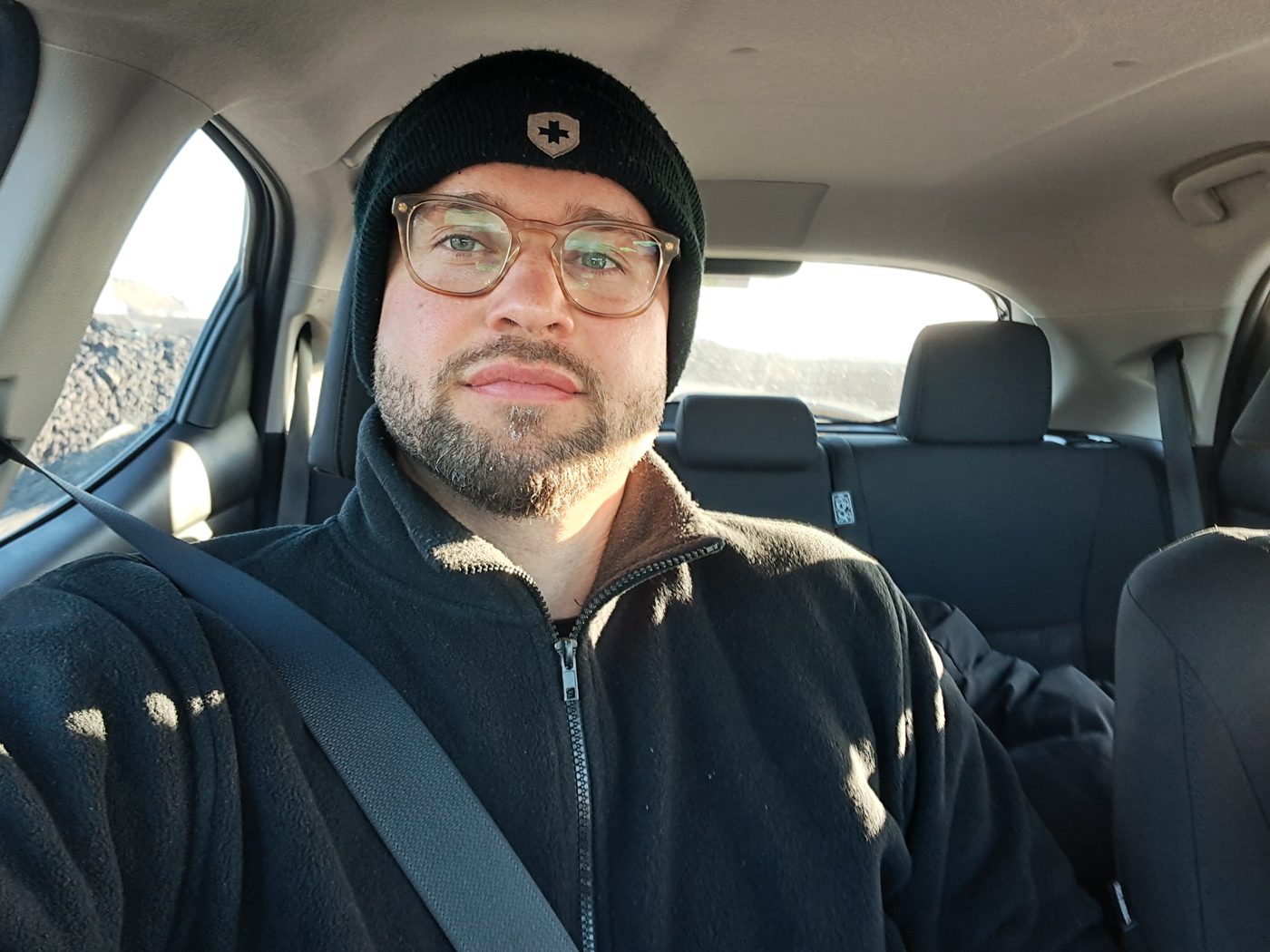 Sitting in the car with a beanie on, calm and content, sun coming through the window