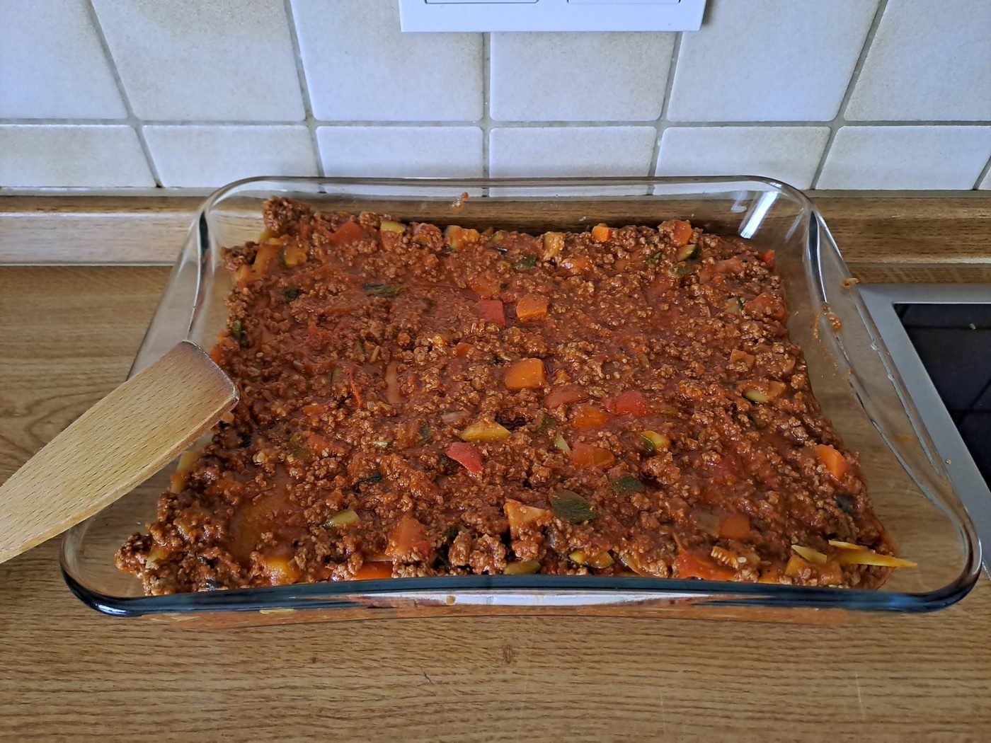 A glass dish of homemade minced beef ragout with vegetables on a family kitchen counter