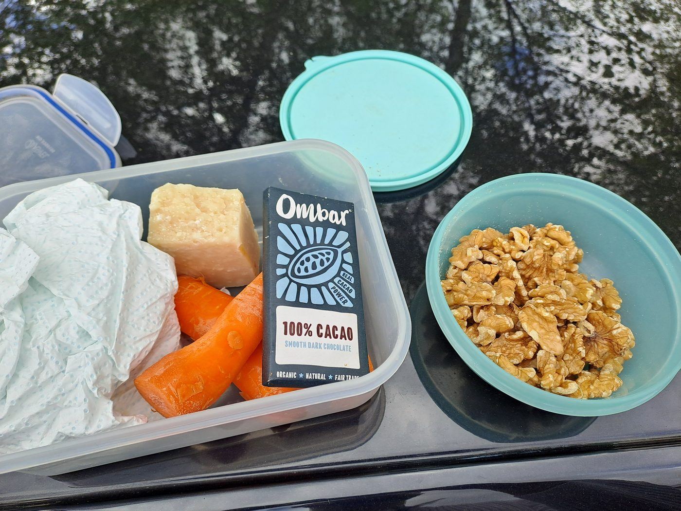 A packed lunch of carrots, Parmigiano and walnuts with a 100% cacao Ombar bar on a car roof