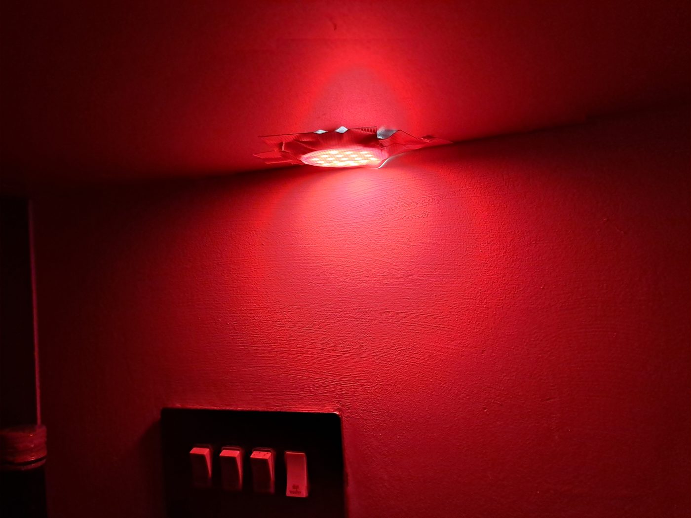An LED light covered with red duct tape, bathing the wall in warm red light
