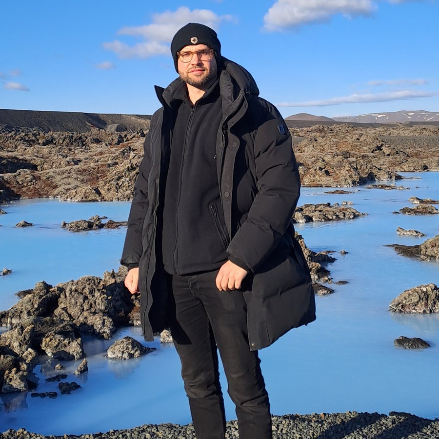 Marvin standing on black lava rock beside the pale blue water of a geothermal lagoon in Iceland