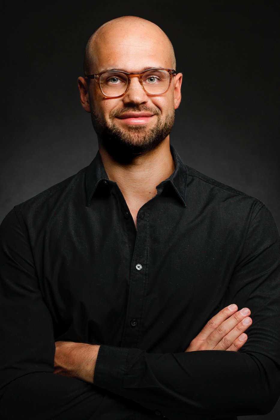 Studio portrait in a black shirt, arms crossed, smiling