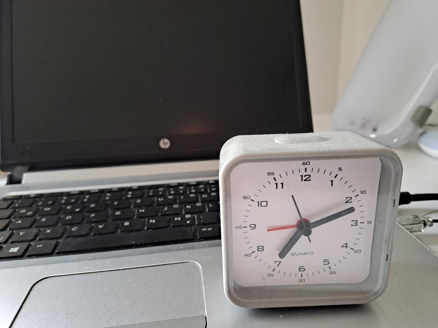 The analog alarm clock standing on a desk next to a laptop