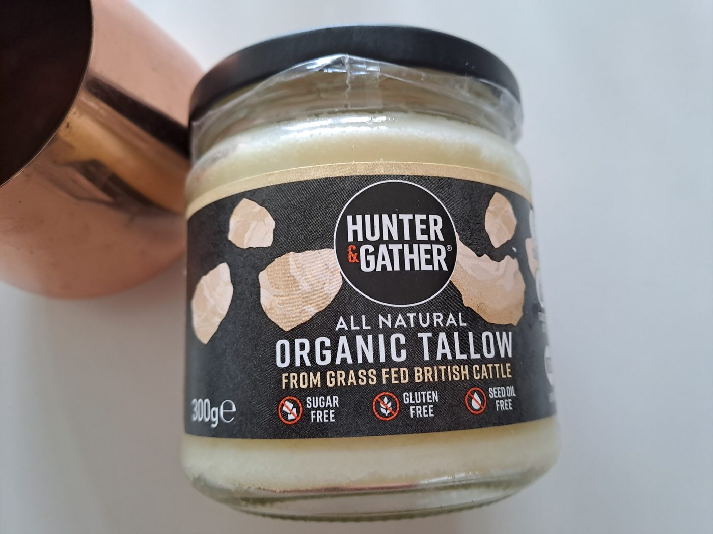 A jar of Hunter and Gather organic grass-fed beef tallow next to a copper cup