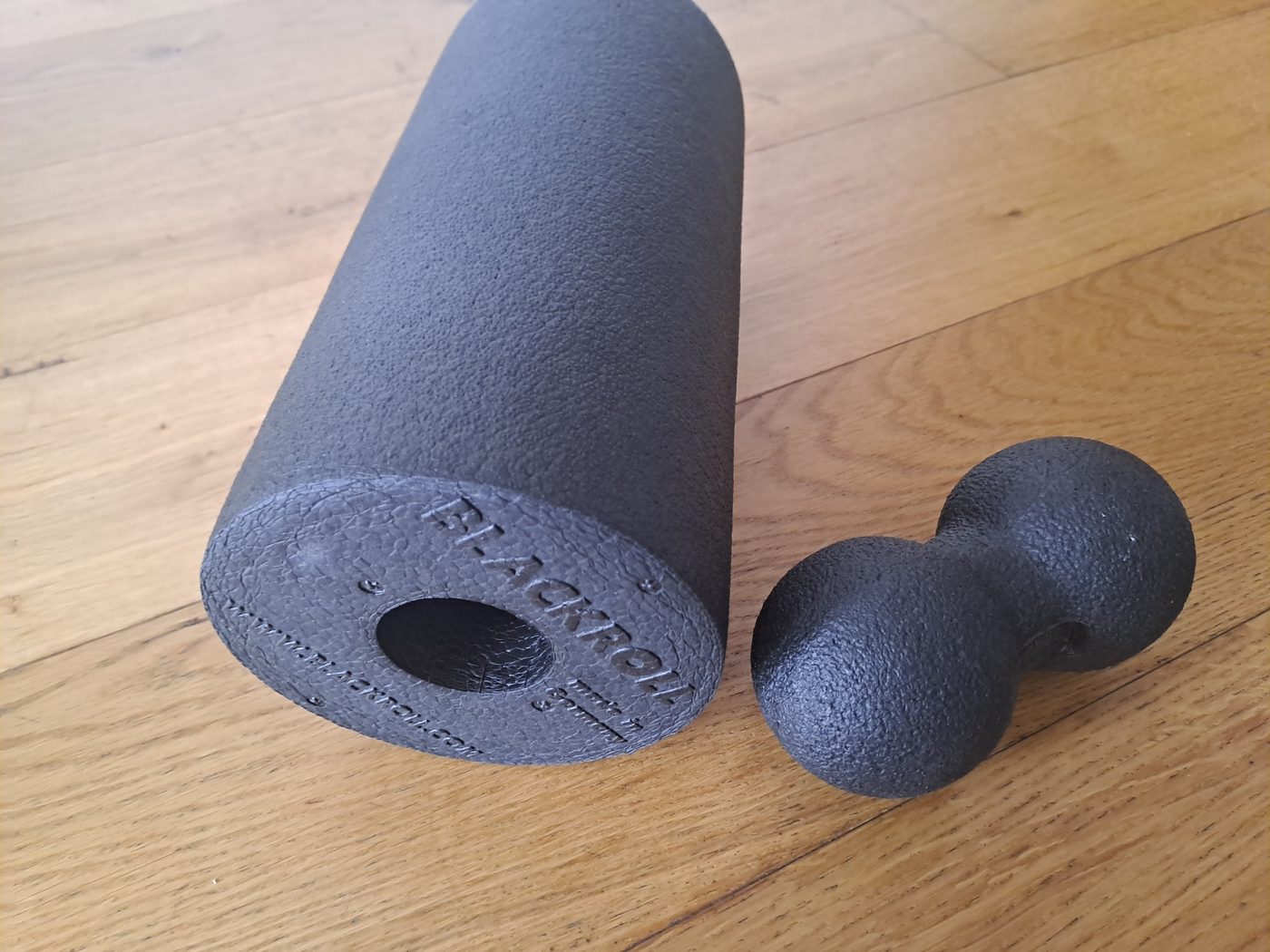 A Blackroll foam roller next to a duoball on a wooden floor