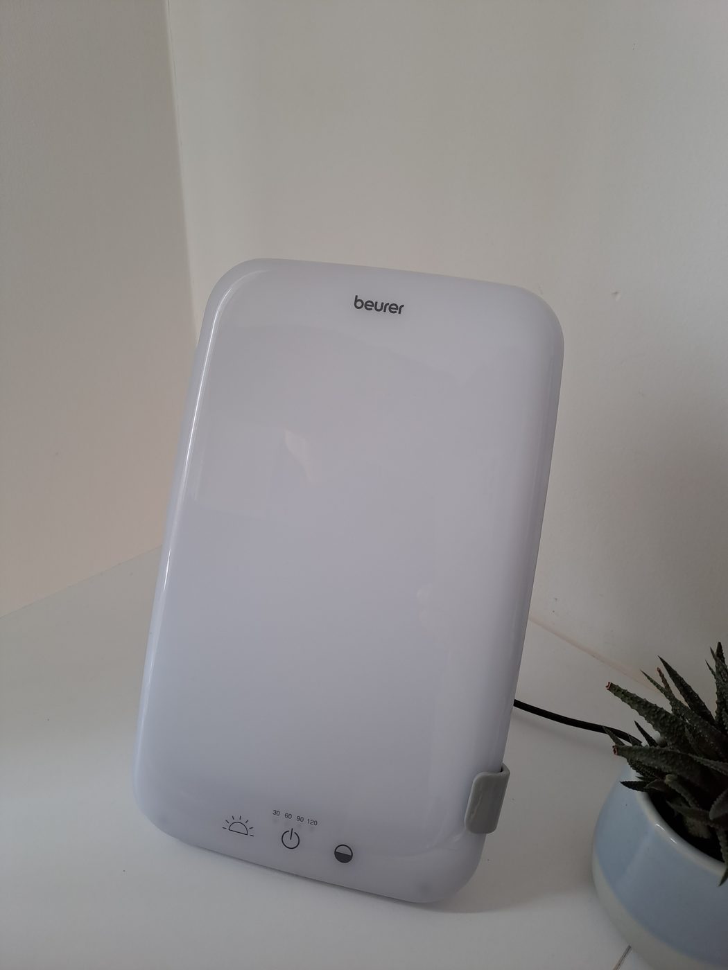 A Beurer daylight therapy lamp on a desk beside a plant