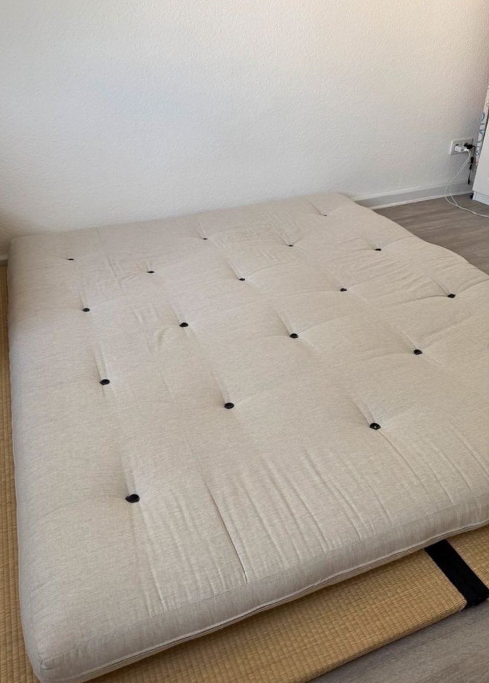 A natural futon mattress laid on a tatami mat on the floor
