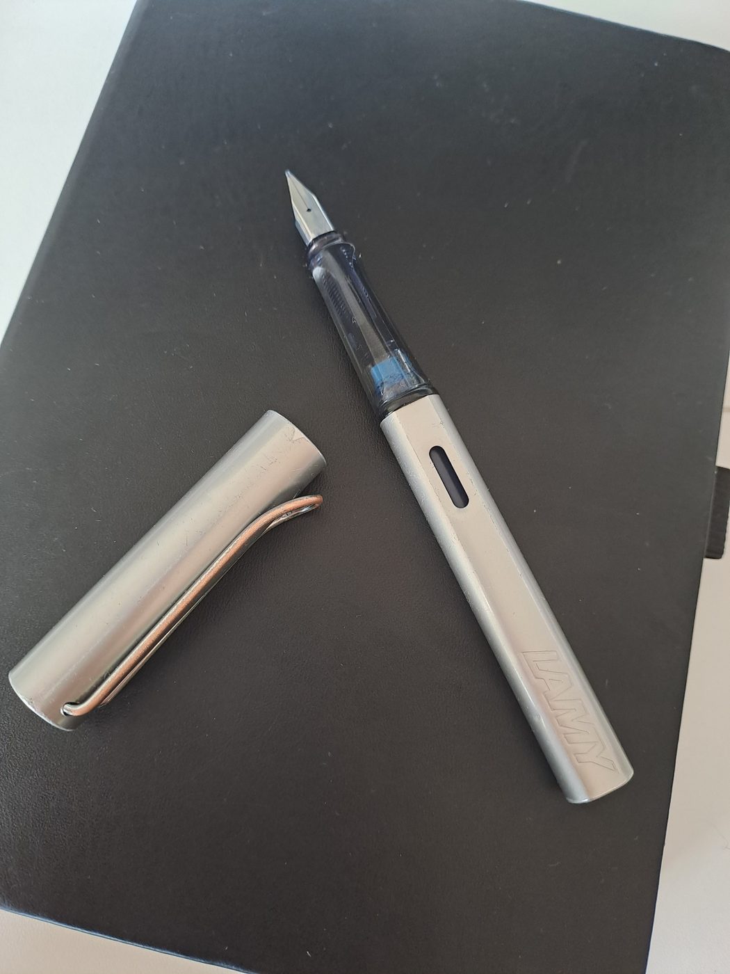 A silver Lamy fountain pen with the cap off on a black notebook