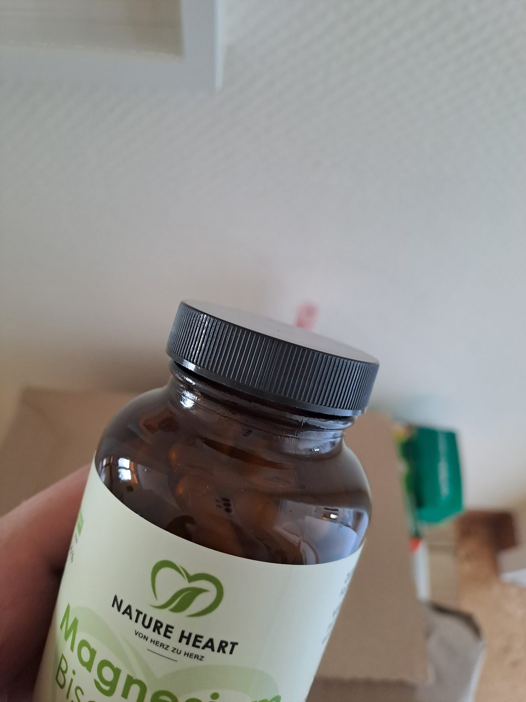 A brown glass bottle of Nature Heart magnesium bisglycinate held in a hand