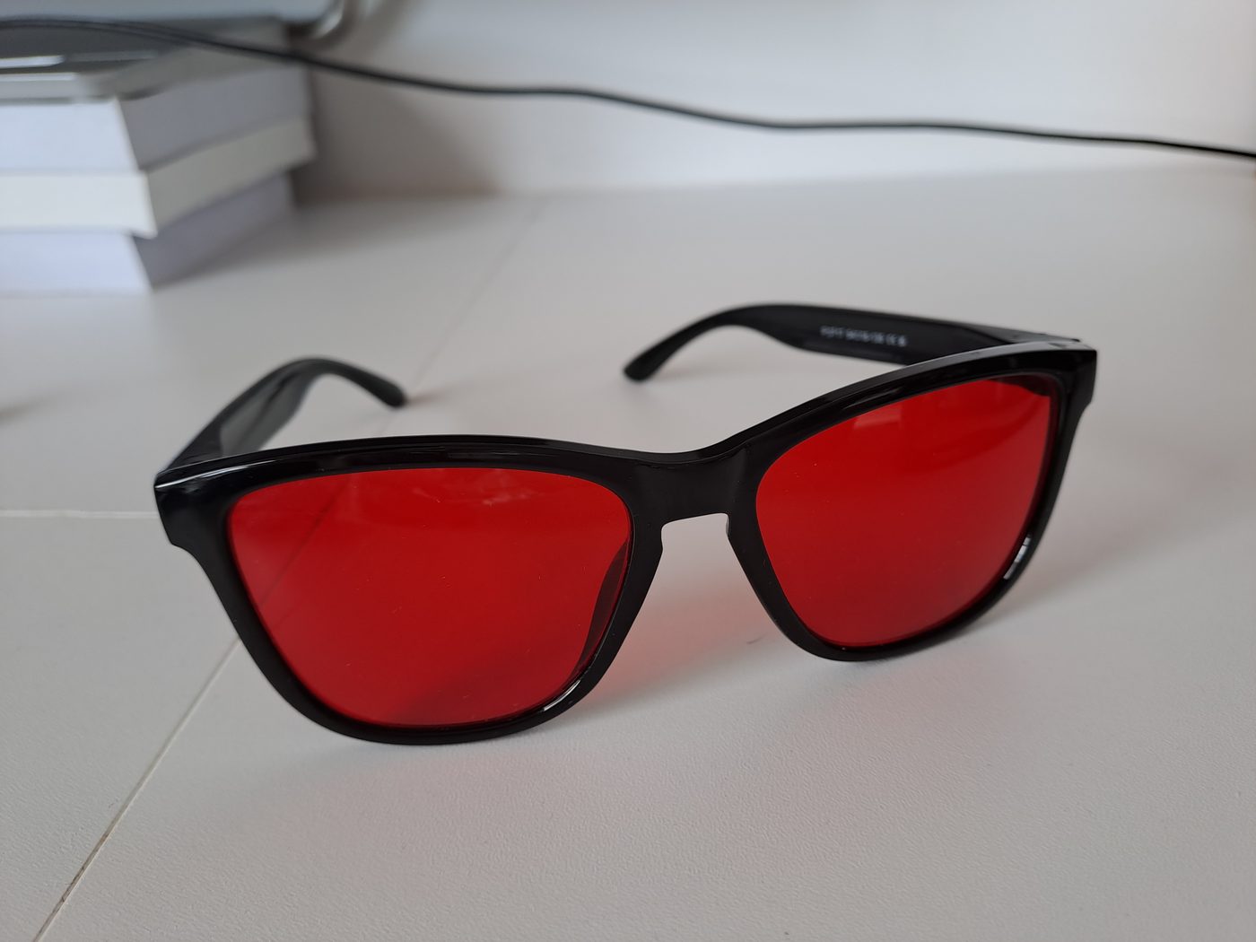 Black glasses with deep red lenses on a white desk