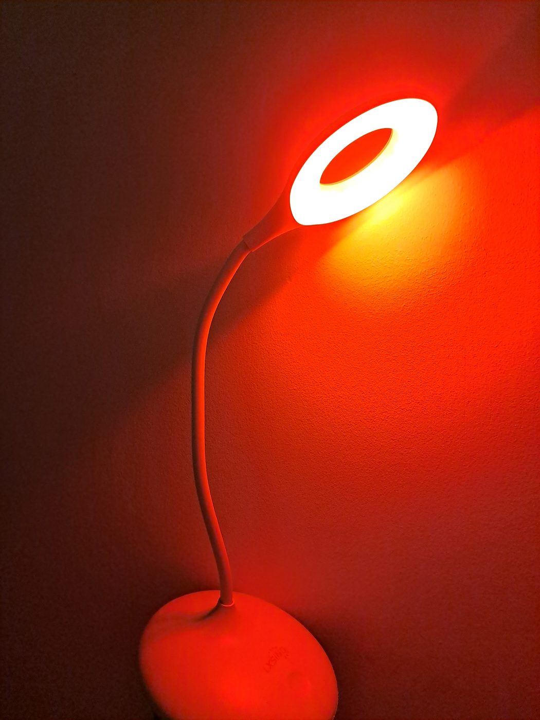 A flexible red light reading lamp glowing warm red against the wall