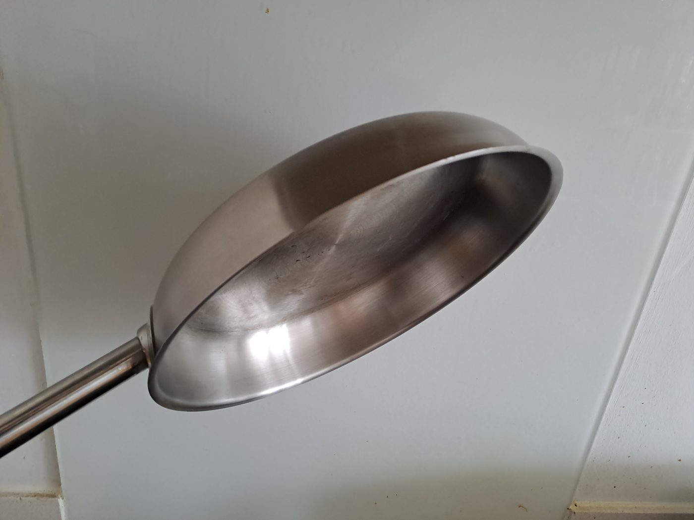 A well-used stainless steel frying pan held up against a tiled wall