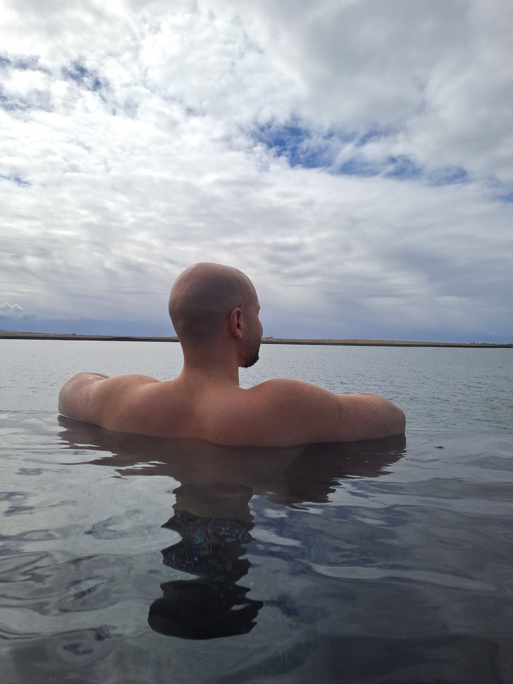 Sitting shoulder deep in open water looking out at the horizon under a wide cloudy sky